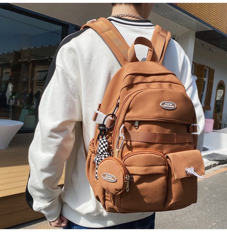 Brown nylon student backpack with laptop compartment, multiple pockets, and checkerboard keychain.