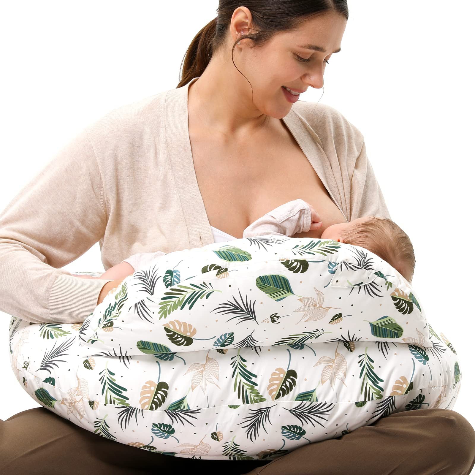 Smiling mother breastfeeding baby using a white nursing pillow with green and brown leaf print.