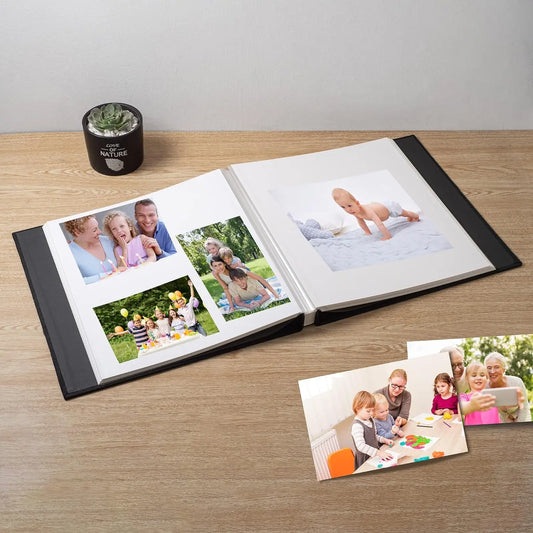 Open black linen photo album with sticky pages displaying family photos on a wooden table.