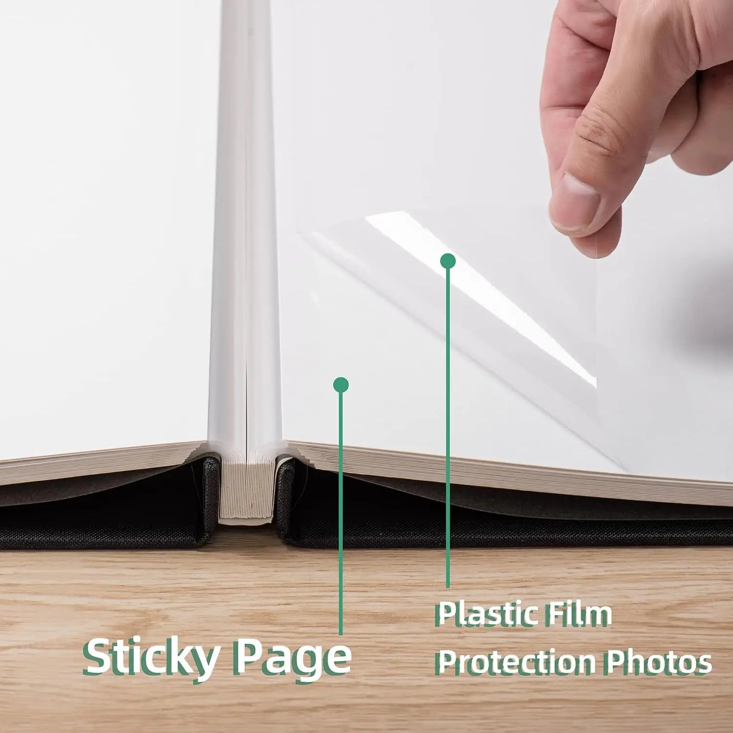 Hand lifting clear plastic film from a sticky white photo album page with a black linen cover.