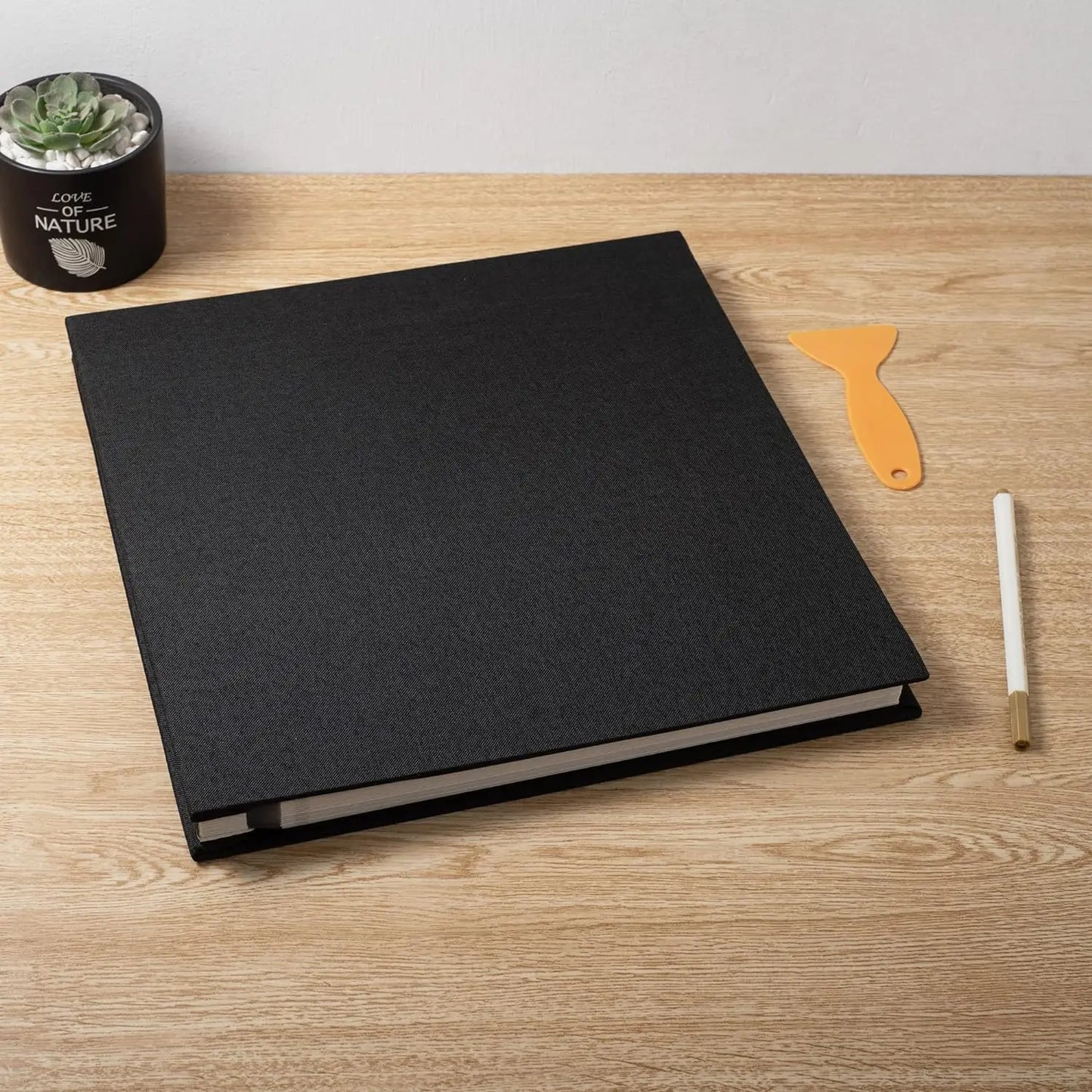Black linen hardcover photo album with 40 sticky pages, on a wooden desk with a succulent and tools.