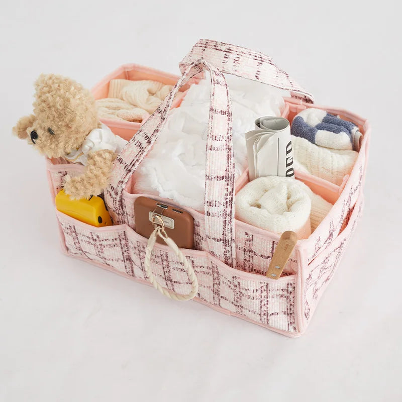 Pink plaid portable baby diaper caddy with multiple compartments, filled with baby essentials and a teddy bear.