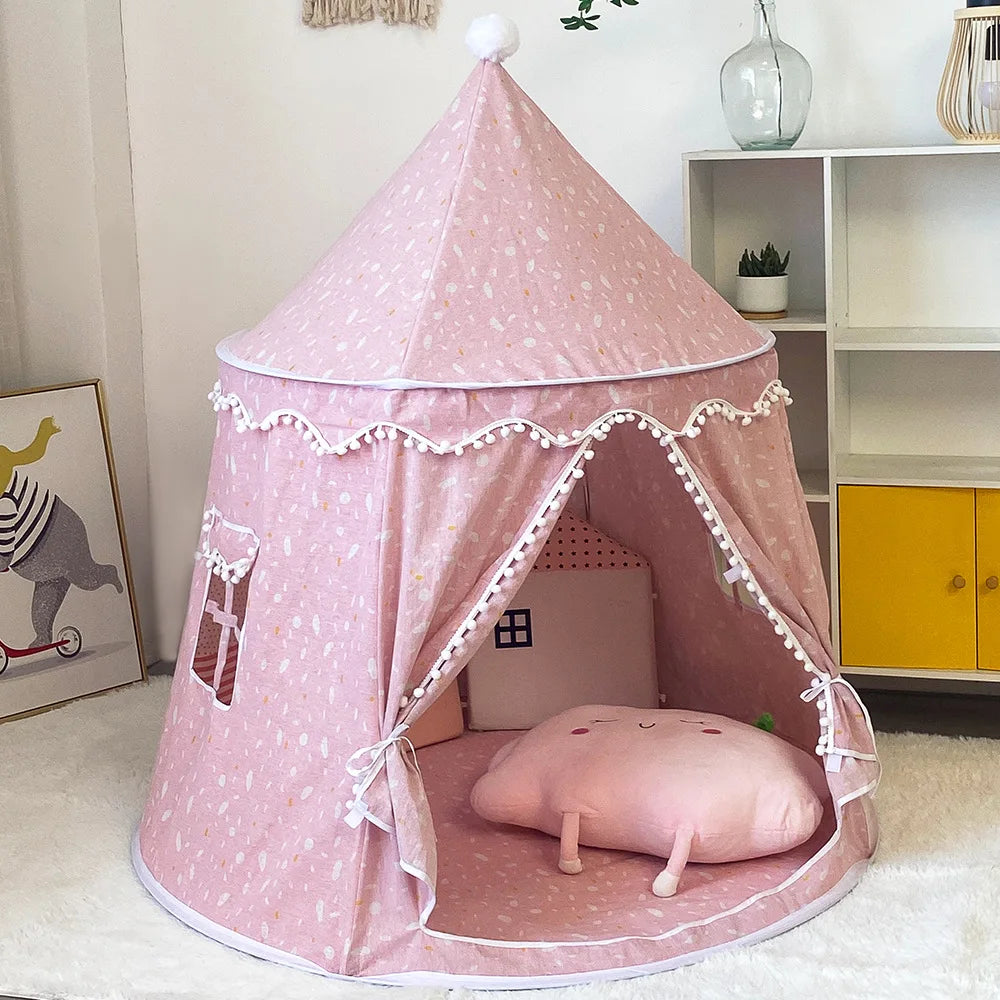 Pink cotton foldable castle play tent for kids with pom-pom trim, window, and open entrance.