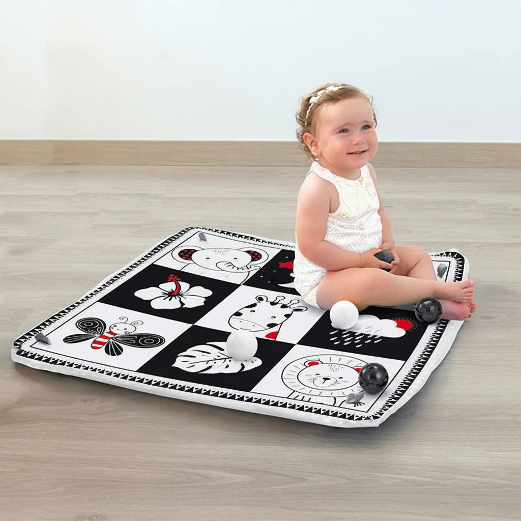 Baby on a black and white activity mat with animal designs and soft balls.