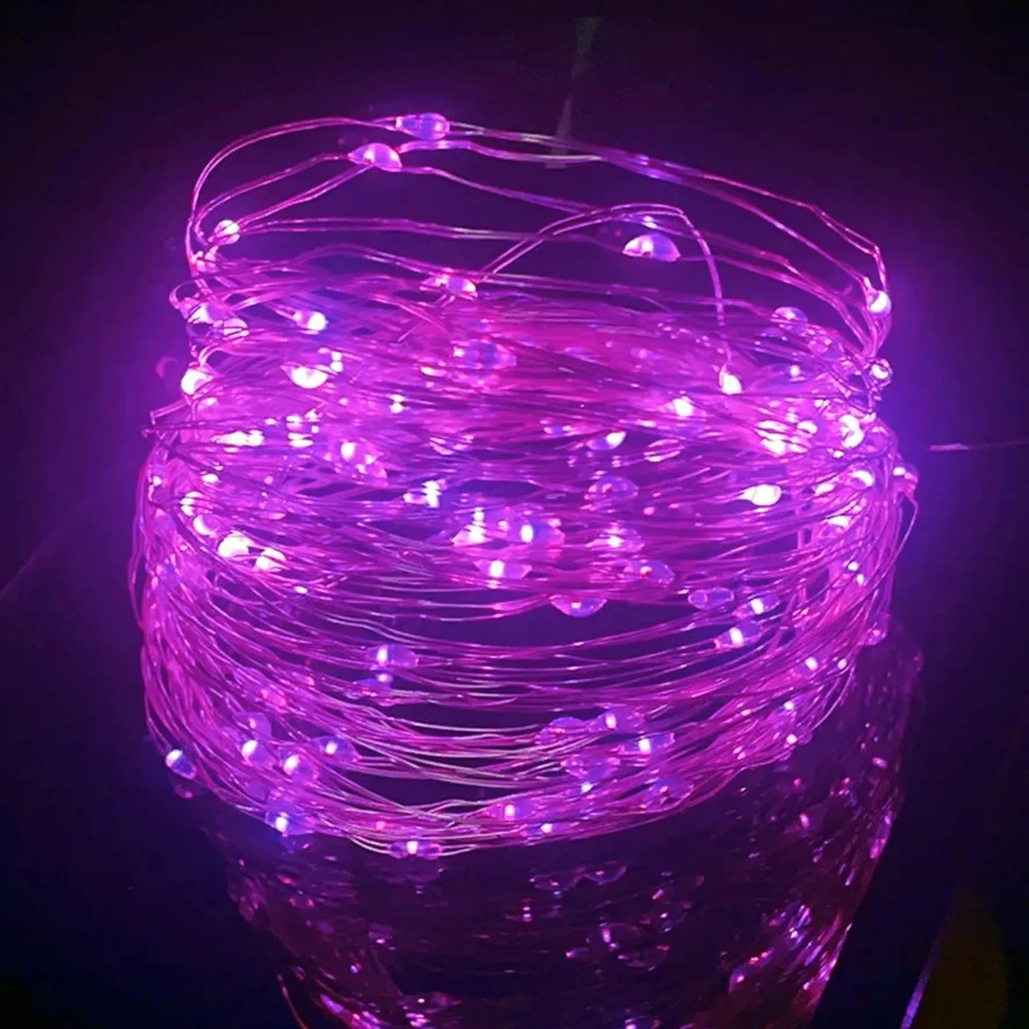Coiled purple LED string lights with tiny bulbs on a flexible copper wire, reflecting on a dark surface.