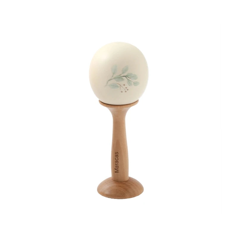 Wooden Montessori maraca with a light cream egg-shaped head featuring a delicate green leaf design.