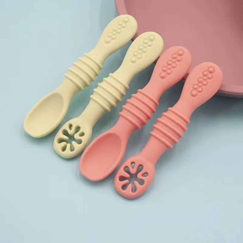 Four soft silicone baby spoons in cream and pink, with ergonomic handles for training and feeding.