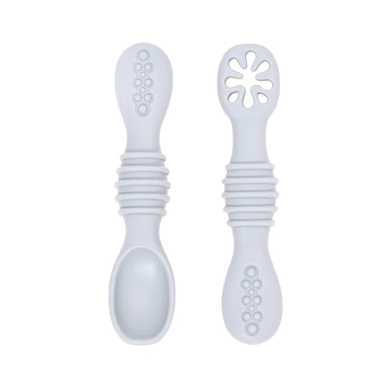 Two light gray silicone baby training spoons with textured handles and soft tips.
