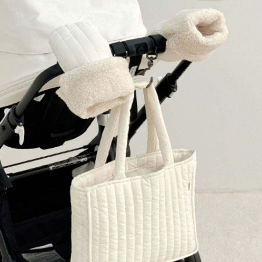 Cream-colored, windproof stroller mittens with soft fleece lining, attached to a black stroller handle.