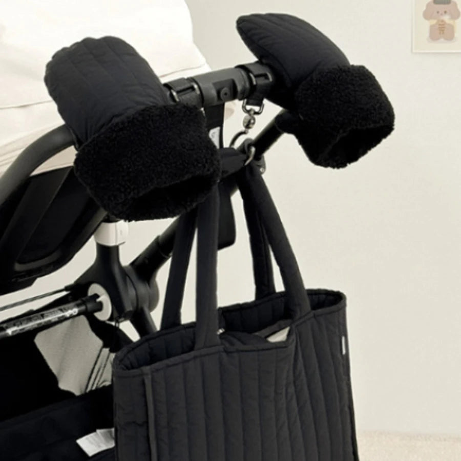 Black quilted stroller hand muffs with soft fleece lining, attached to a stroller handle.