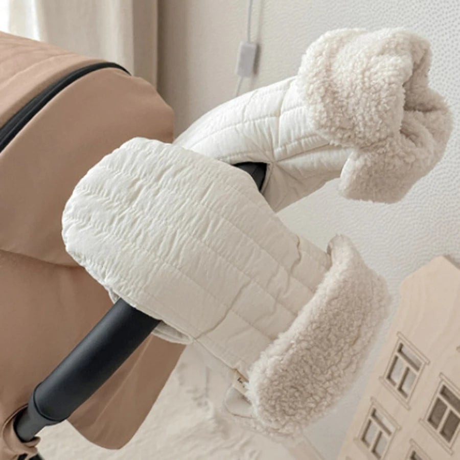 Quilted cream stroller mittens with plush fleece lining attached to a black stroller handle.