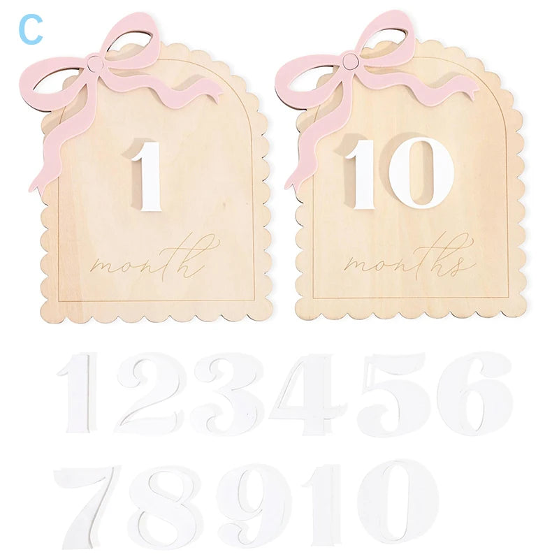 Wooden baby milestone cards with pink bows and interchangeable white numbers for photography.