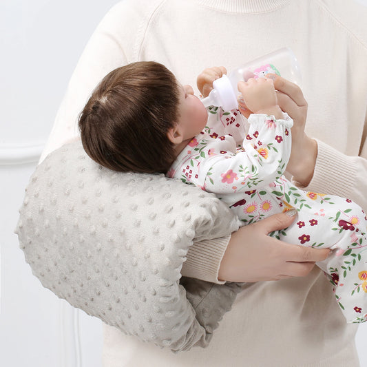 Ergonomic gray textured nursing arm pillow supporting a baby doll being bottle-fed.