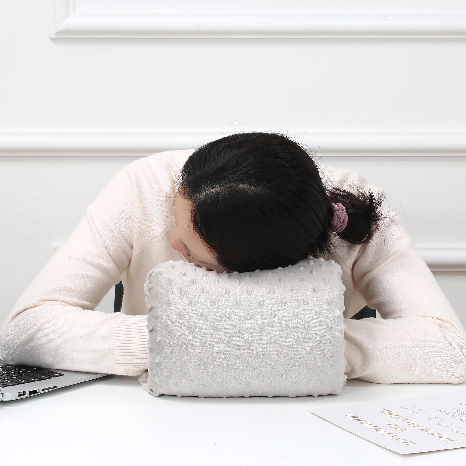 Woman resting head on a soft, white textured nursing arm pillow on a desk.