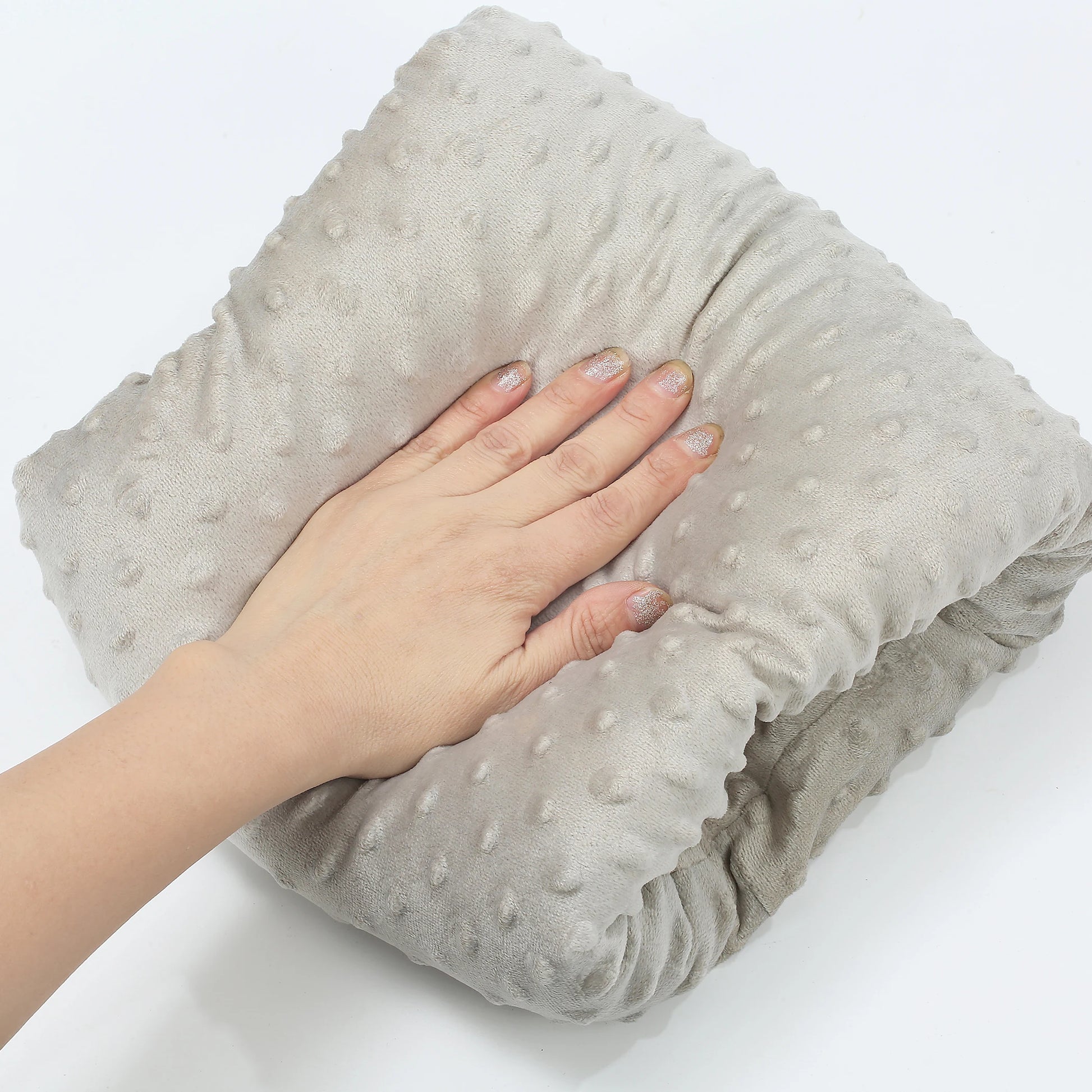 Hand touching a soft, light gray ergonomic nursing arm pillow with raised dot texture.