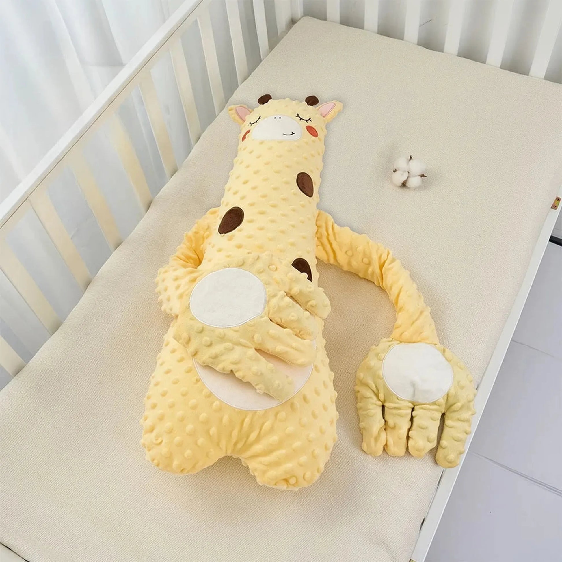 Yellow giraffe baby soothing pillow with a gentle patting mechanism and remote control, in a crib.
