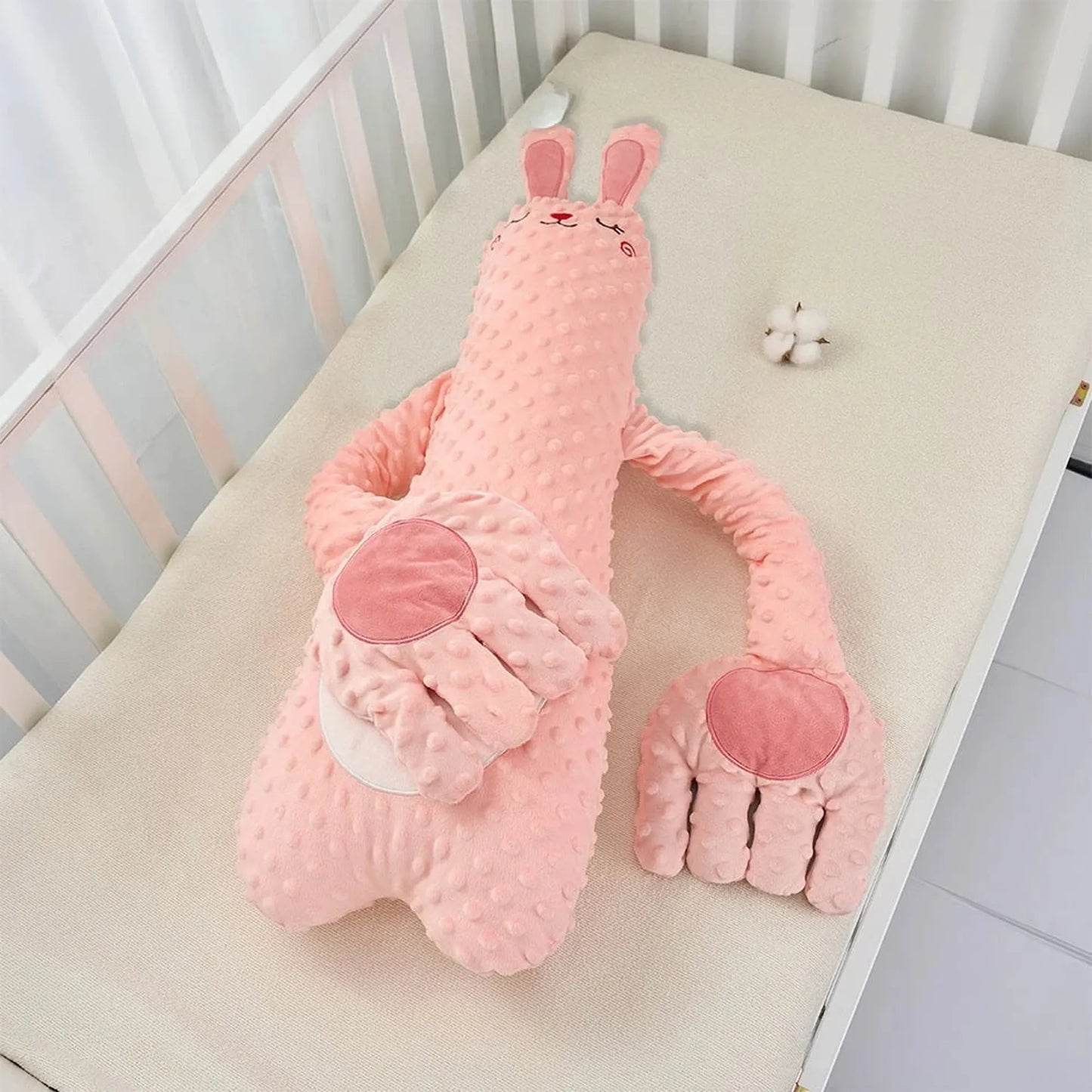 Pink bunny baby soothing pillow with textured fabric and large hand-shaped arms in a crib.