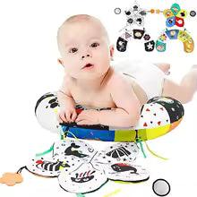 Baby on tummy time with a high-contrast black and white developmental pillow and sensory toys.