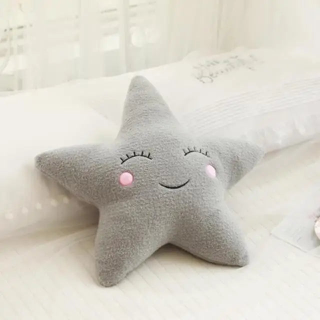 Soft gray star-shaped decorative baby pillow with embroidered sleepy eyes and pink cheeks.