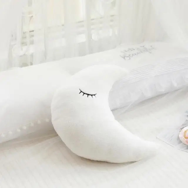 Soft white crescent moon pillow with embroidered sleeping eyes, perfect for nursery decor.