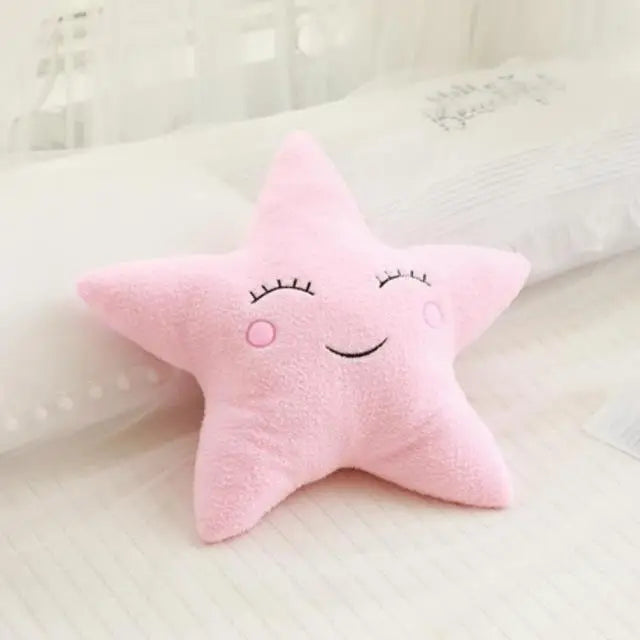 Soft pink star-shaped decorative pillow with embroidered sleepy eyes and a smile, ideal for a baby's room.