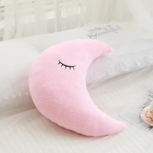 Soft pink crescent moon decorative pillow with embroidered sleeping eyes for a baby's room.