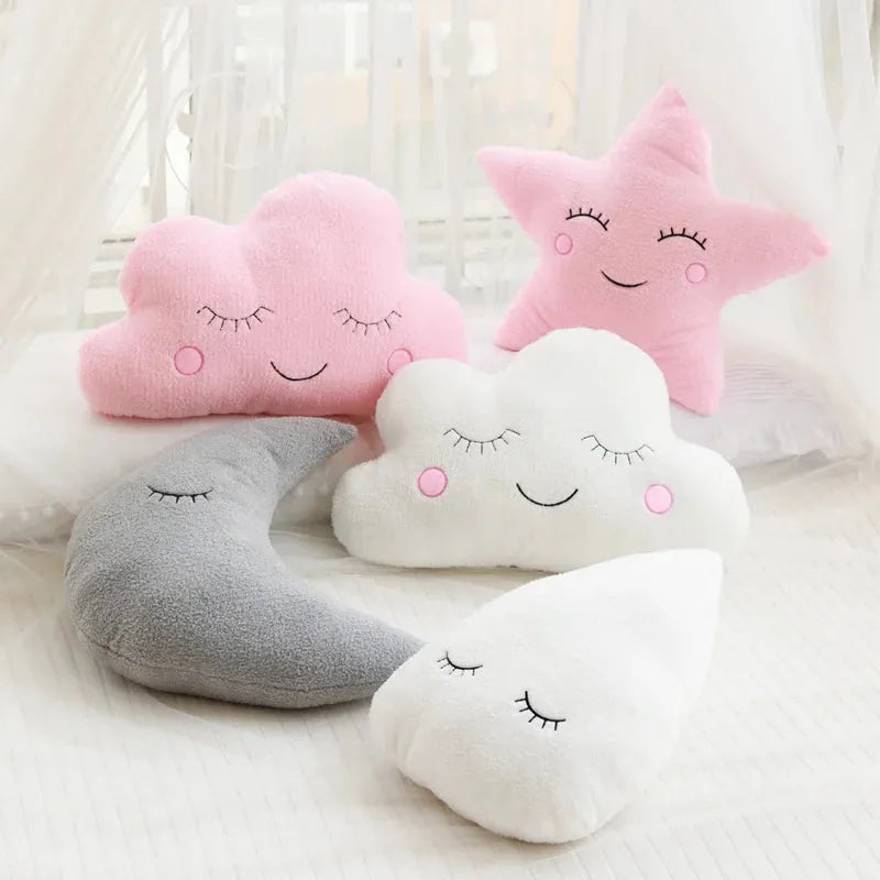 Soft plush nursery pillows: pink cloud, white cloud, pink star, gray moon, and white raindrop with sleepy faces.