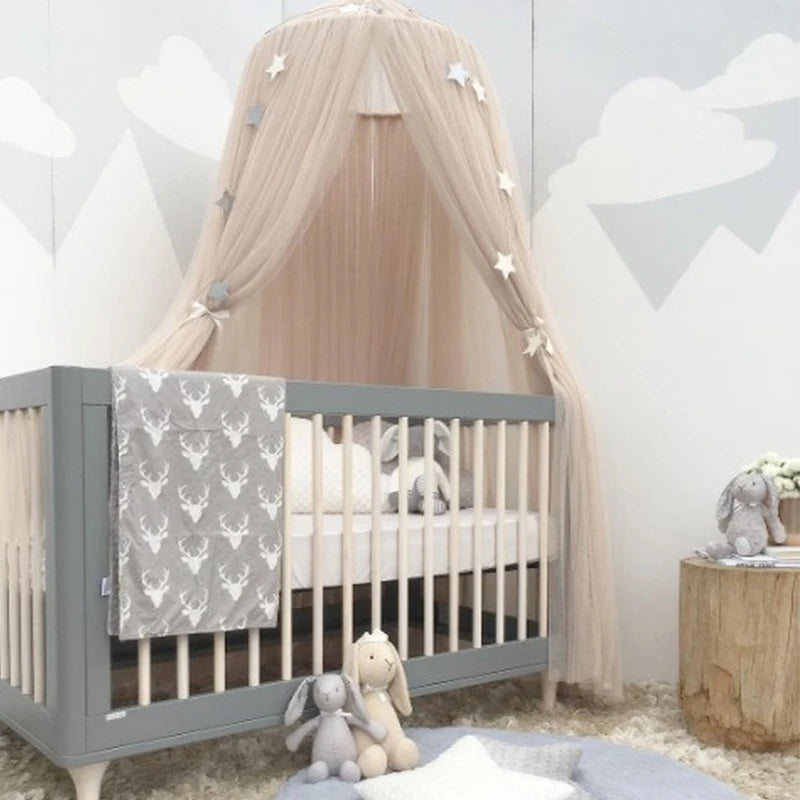 Beige tulle baby crib canopy with silver stars, hanging over a gray crib with a deer-print blanket.
