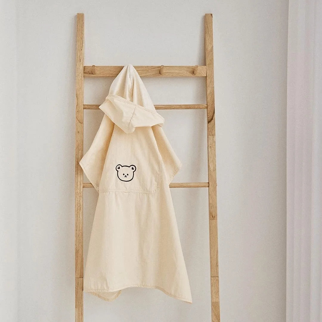 Cream polyester baby carrier and stroller cover with a cute bear design and hood, hanging on a wooden ladder.