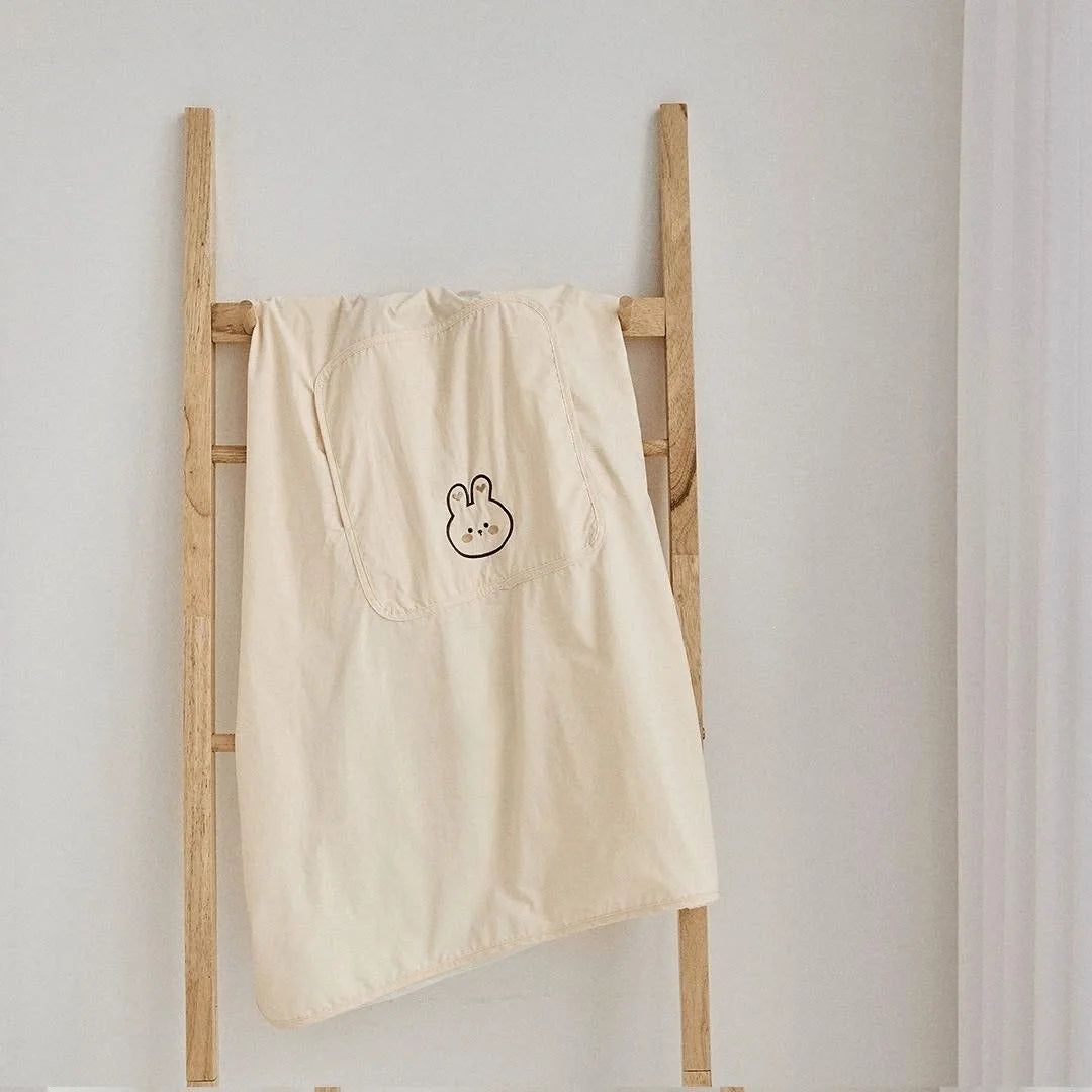 Cream polyester baby carrier/stroller cover with a cute embroidered bunny face and hood, hanging on a wooden ladder.