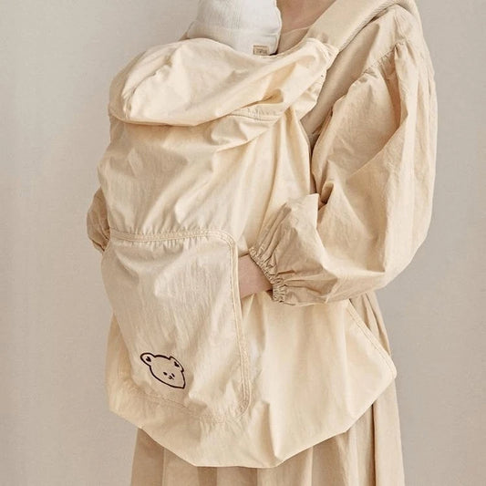 Beige polyester baby carrier cover with a cute bear design and hood, worn over a baby.