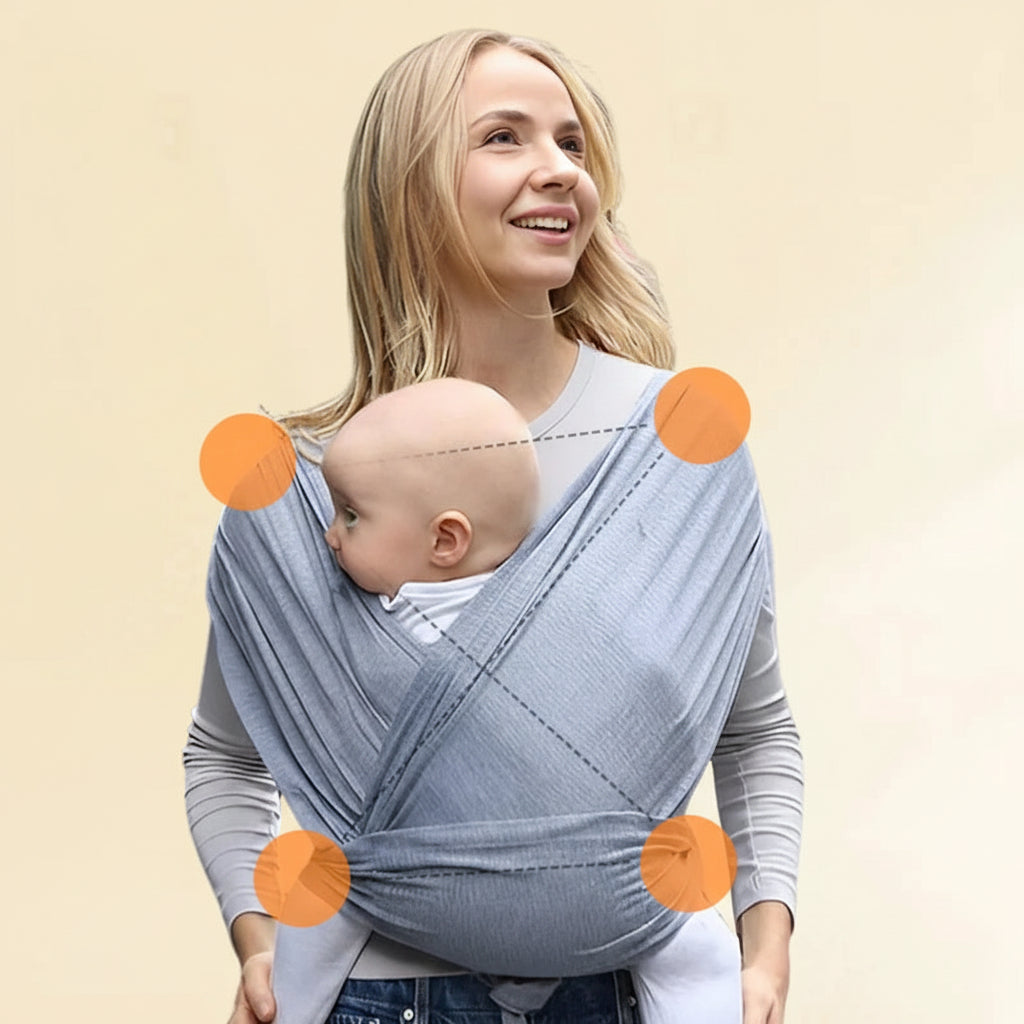 Smiling mother carrying baby in a soft, grey ergonomic cotton baby wrap with cross shoulder straps.