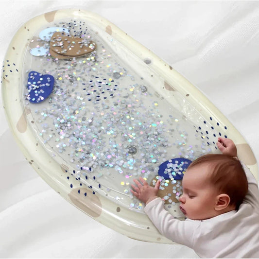 Inflatable baby water play mat with glitter and shapes, next to a sleeping infant.
