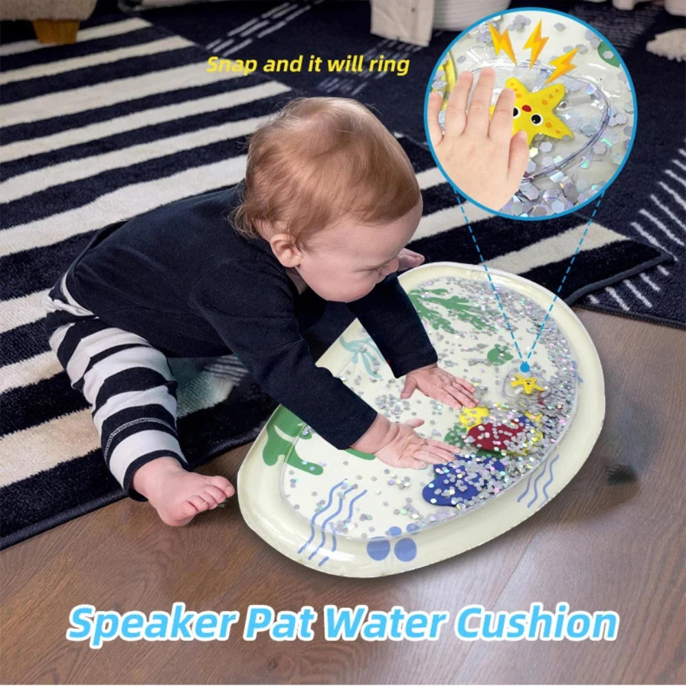 Baby on a striped rug playing with an oval inflatable water mat featuring floating colorful sea creatures and glitter.