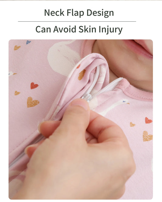 Close-up of a hand zipping a pink cotton baby sleep sack with heart and unicorn prints, showing the neck flap design.