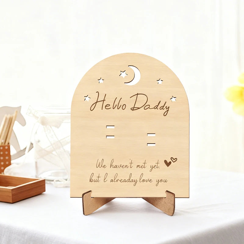 Arched natural wood pregnancy announcement sign with "Hello Daddy" and "We haven't met yet, but I already love you" text.