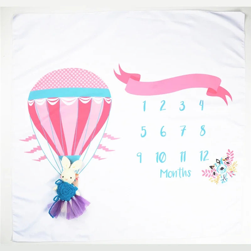 Soft white polyester baby milestone blanket with pink hot air balloon, monthly numbers, and bunny toy.
