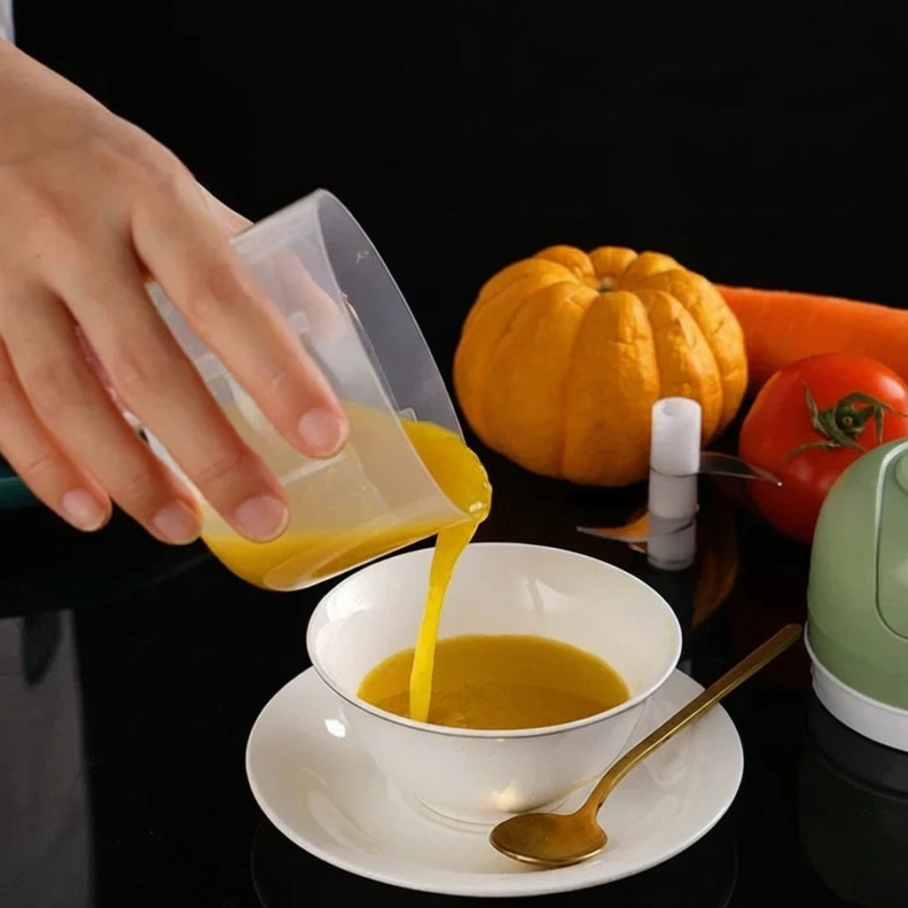Hand pouring yellow baby food puree from a clear cup into a white bowl with a gold spoon.