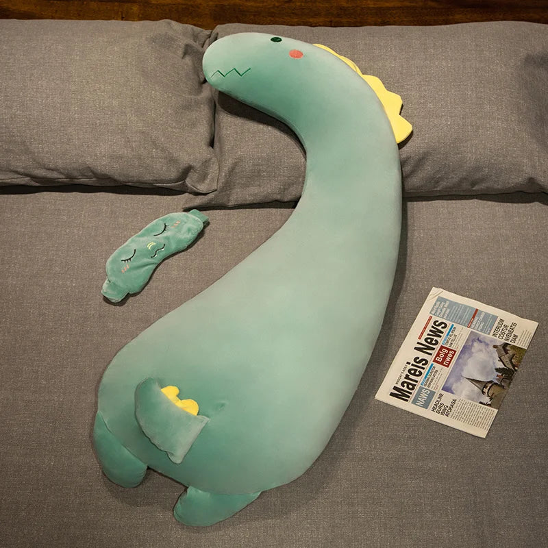 Soft mint green dinosaur plush pillow with yellow accents, on a gray bed.