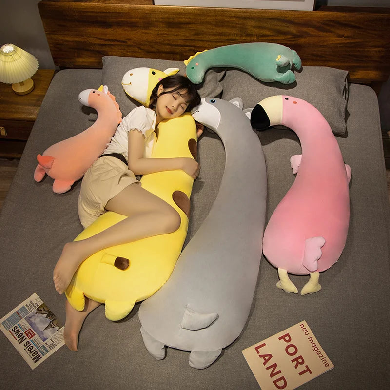 Woman sleeping with large, soft plush animal pillows: yellow banana, grey husky, pink flamingo, orange unicorn, green dinosaur.