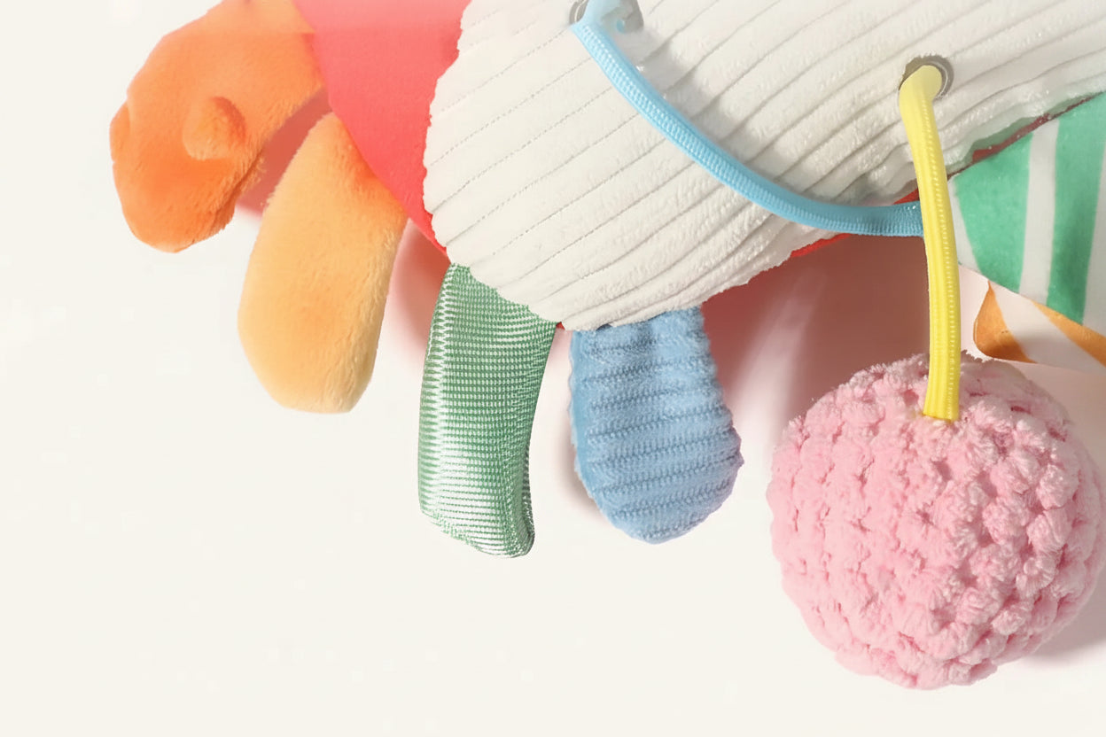 Colorful plush baby crib toy with pull mechanism, featuring dotted plush, soft plush, corduroy, and pineapple grid textures.