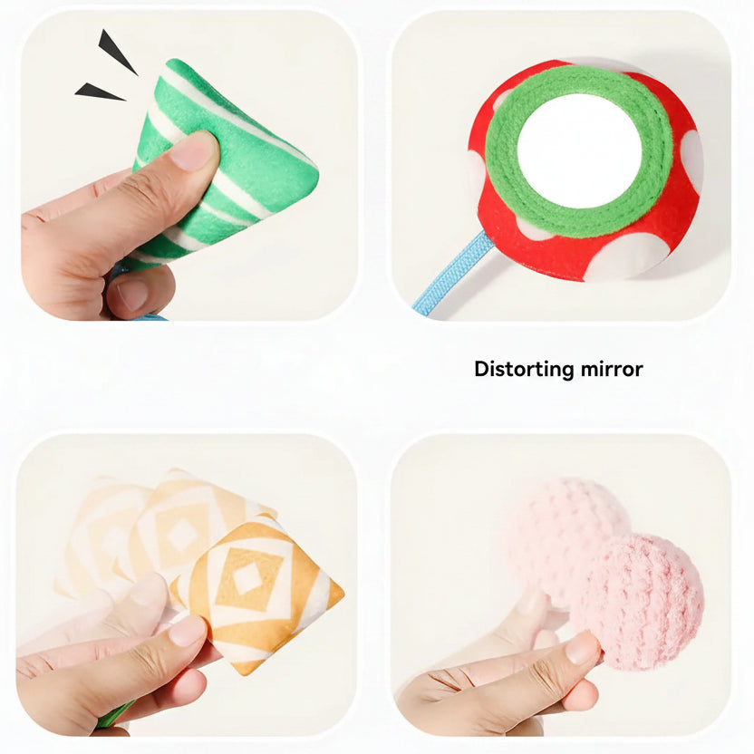 Close-up of a baby crib hanging toy with pull mechanism, showing soft fabric elements: green cone, red mirror, patterned square, and pink ball.