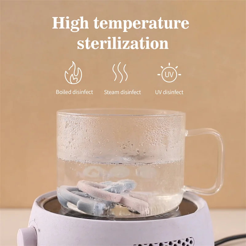Pink and blue silicone bunny teether being sterilized in boiling water within a clear glass mug.