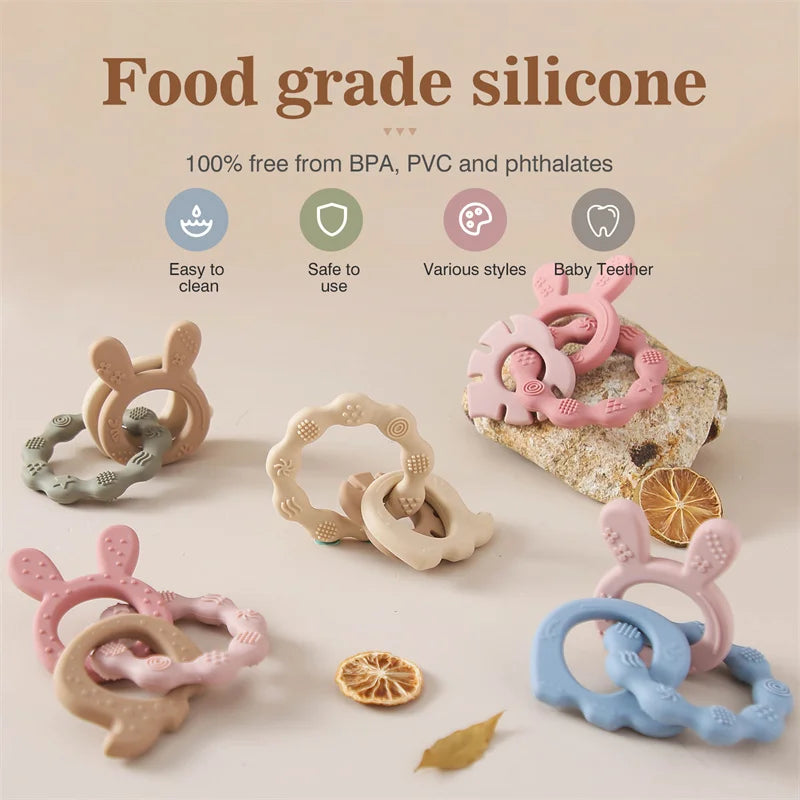 Food-grade silicone baby teether rings in pastel pink, blue, beige, and green, shaped like cute bunnies.