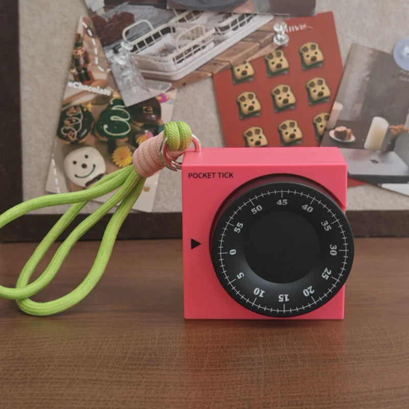 Pink square visual timer with a black dial, white numbers, and a green lanyard, on a wooden surface.
