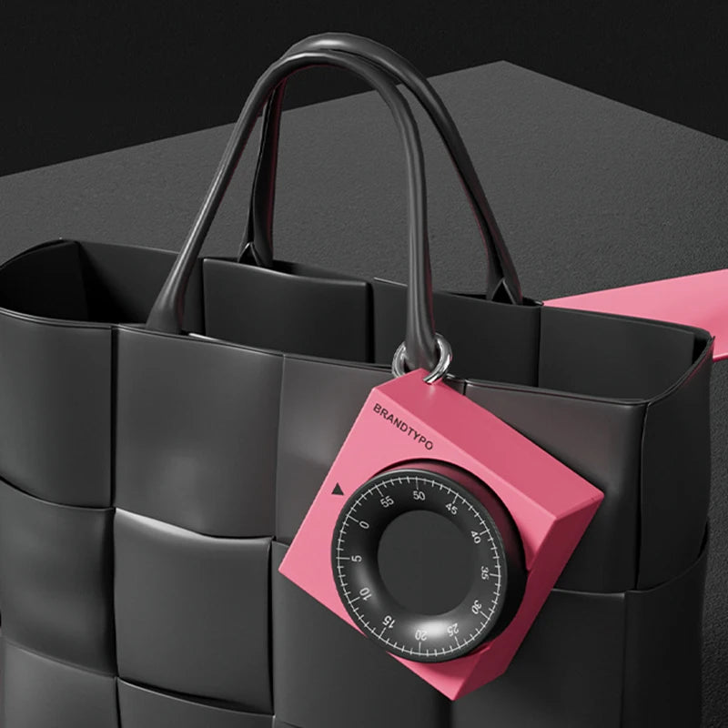 Pink square visual timer with a black dial, hanging from a black woven tote bag.