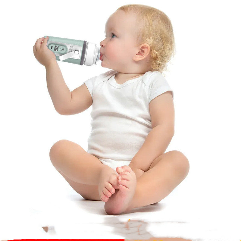 Baby in white onesie drinking from a portable USB bottle warmer in light green.