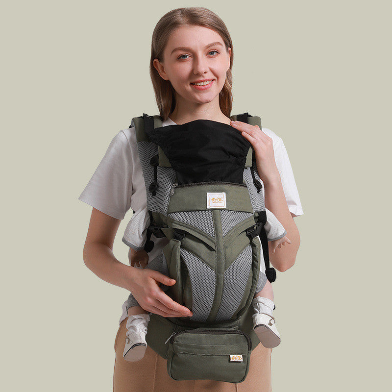 Woman smiling, wearing an olive green ergonomic cotton baby carrier with mesh accents and a black headrest.