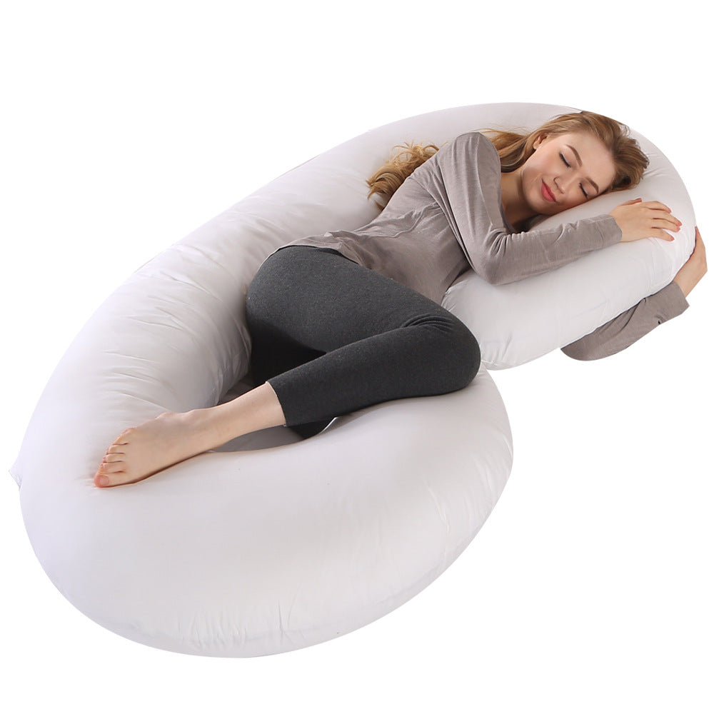 Woman sleeping soundly on a large white C-shaped pregnancy pillow, providing full body support.