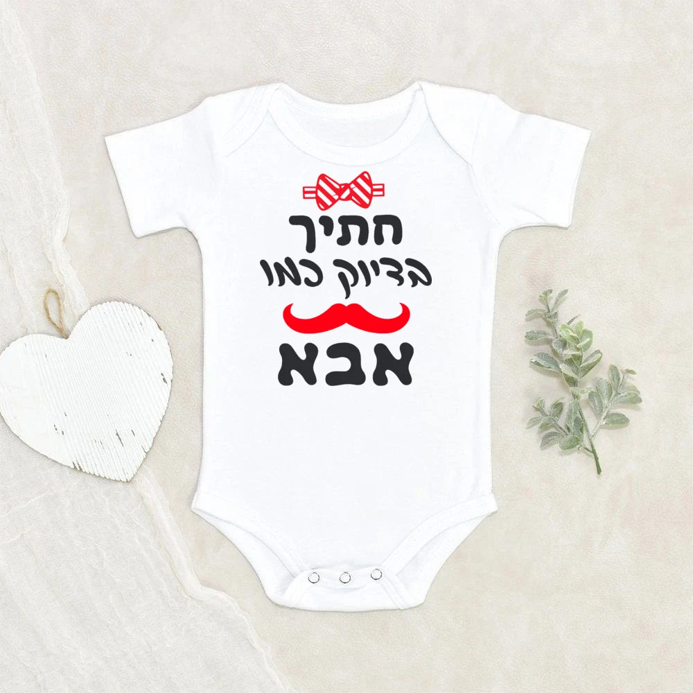 White short-sleeve baby bodysuit with "Handsome like Dad" in Hebrew, a red bow tie, and mustache graphic.